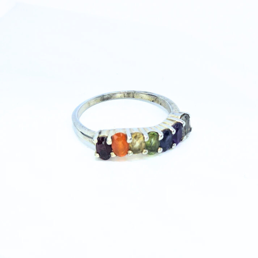 A sterling silver ring with seven multicolored chakra stones arranged in a line.
