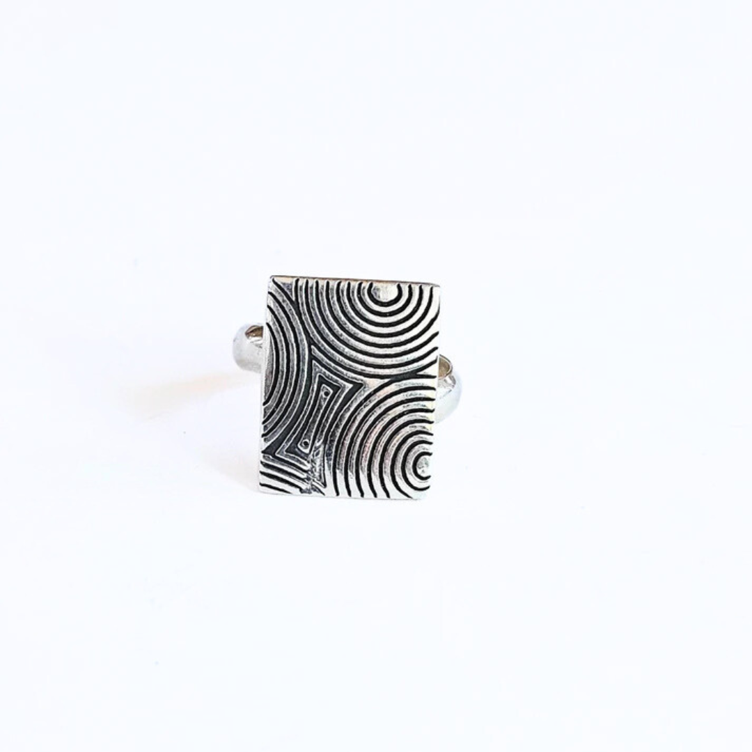 A silver ring with a patterned swirl design, featuring a square-shaped band with a detailed geometric pattern.